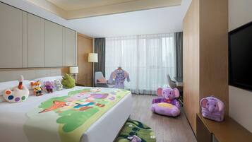 A hotel room with a bed, a desk, a chair, a TV, and various children's toys.