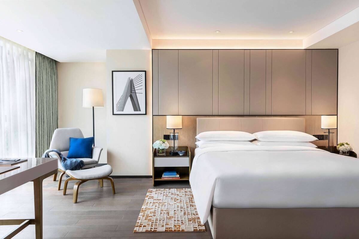 Ein modernes Hotelzimmer mit einem großen Bett, einem Schreibtisch, einem Stuhl und einem Nachttisch mit Lampen.