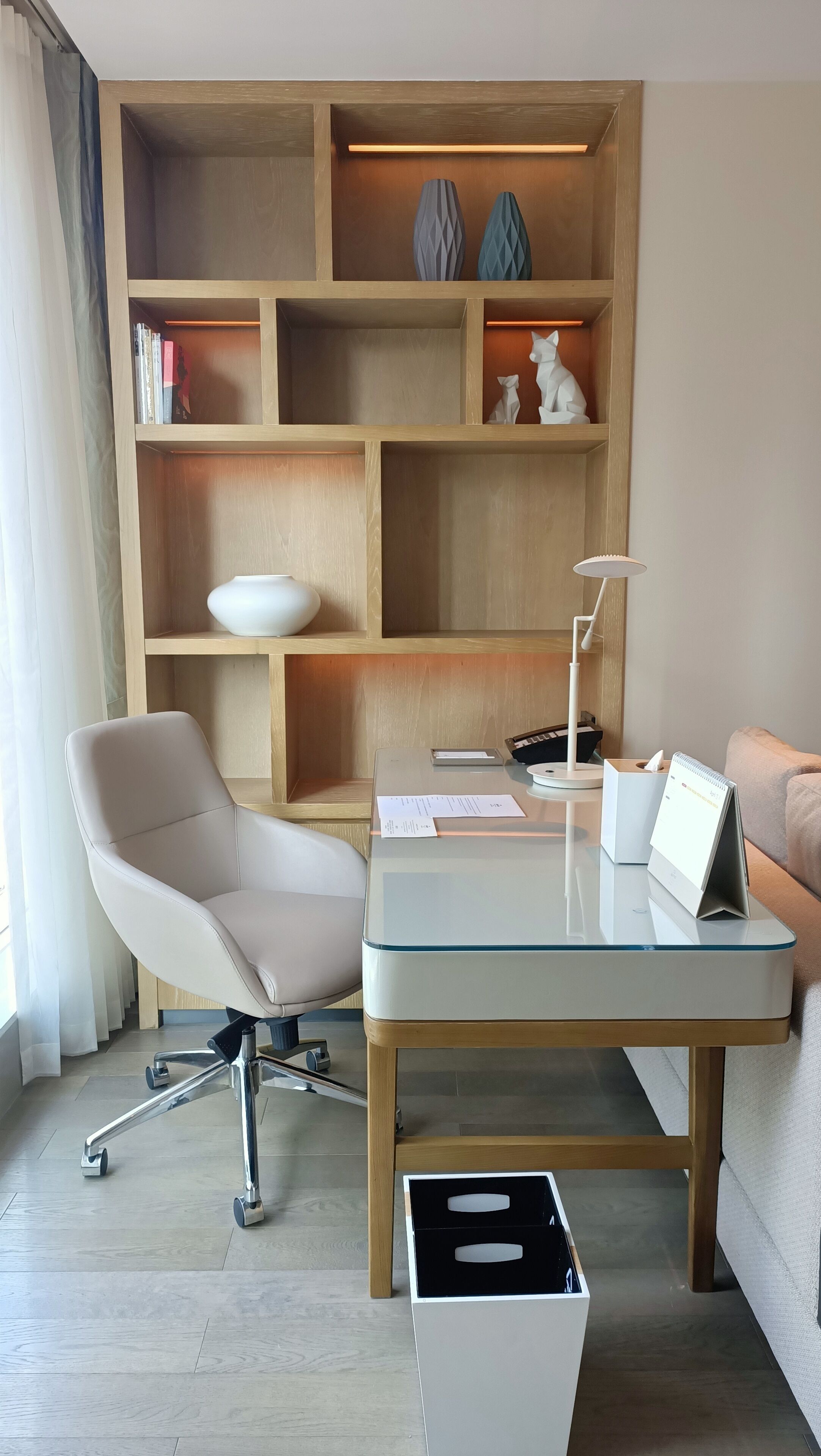 A modern office space with a desk, chair, and shelving unit.