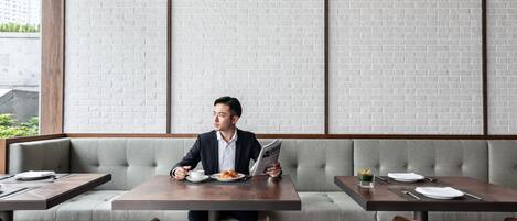 A man sitting at a table in a restaurant with a brick wall background, a sofa, and a window.