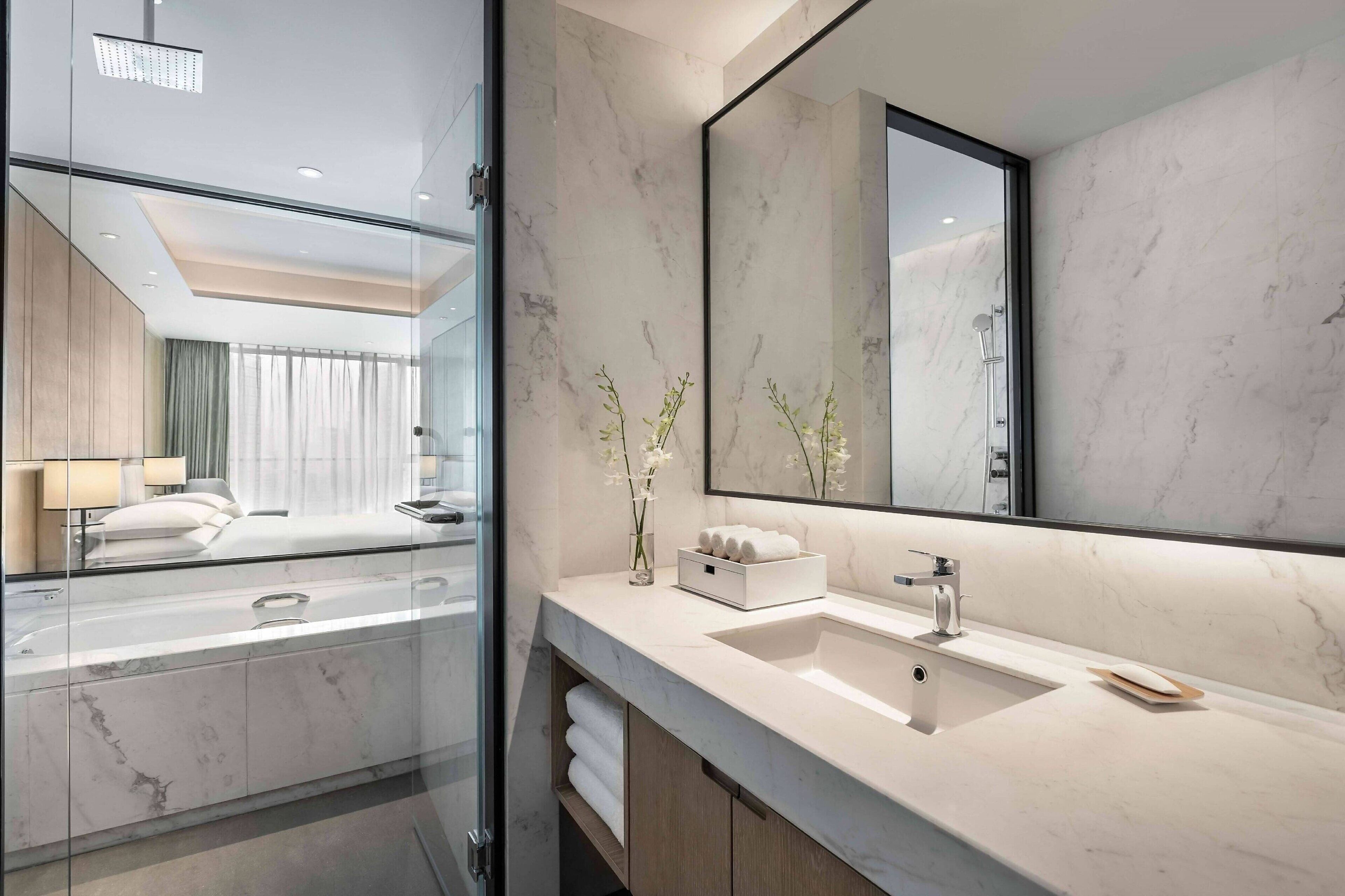 A modern bathroom with a large mirror, marble countertops, and a glass shower enclosure.