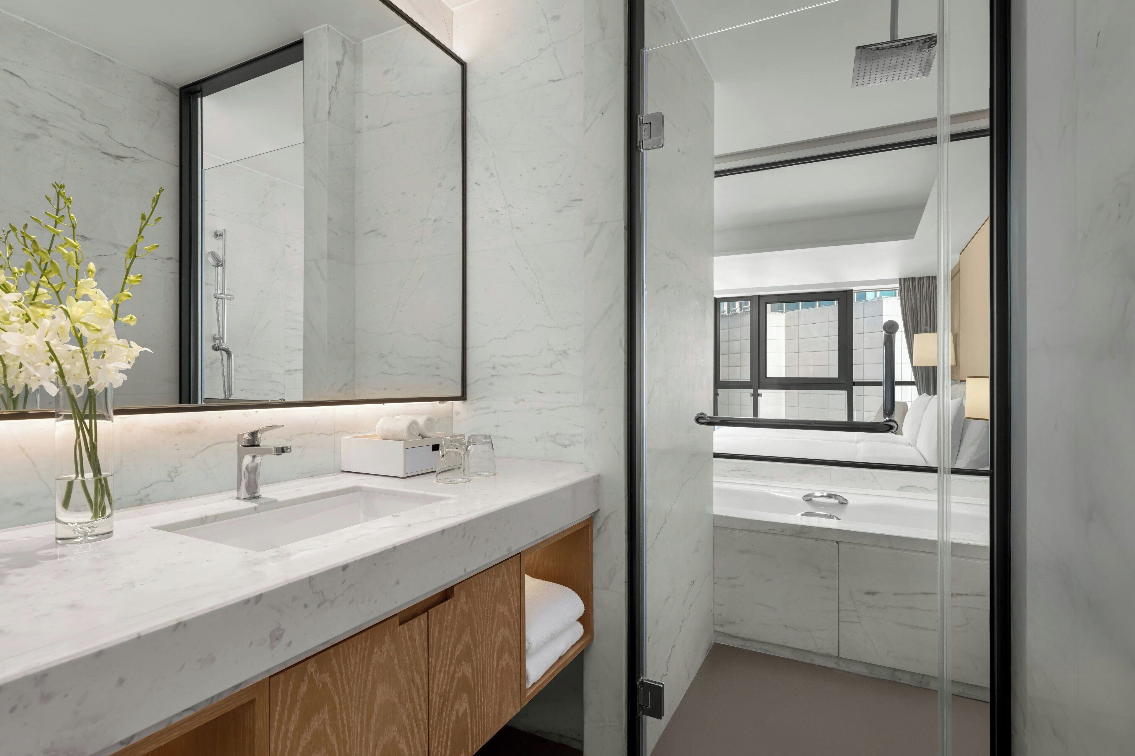 A modern bathroom with a glass shower enclosure, marble countertops, and a large mirror.