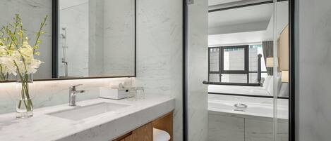 A modern bathroom with a glass shower enclosure, marble countertops, and a large mirror.
