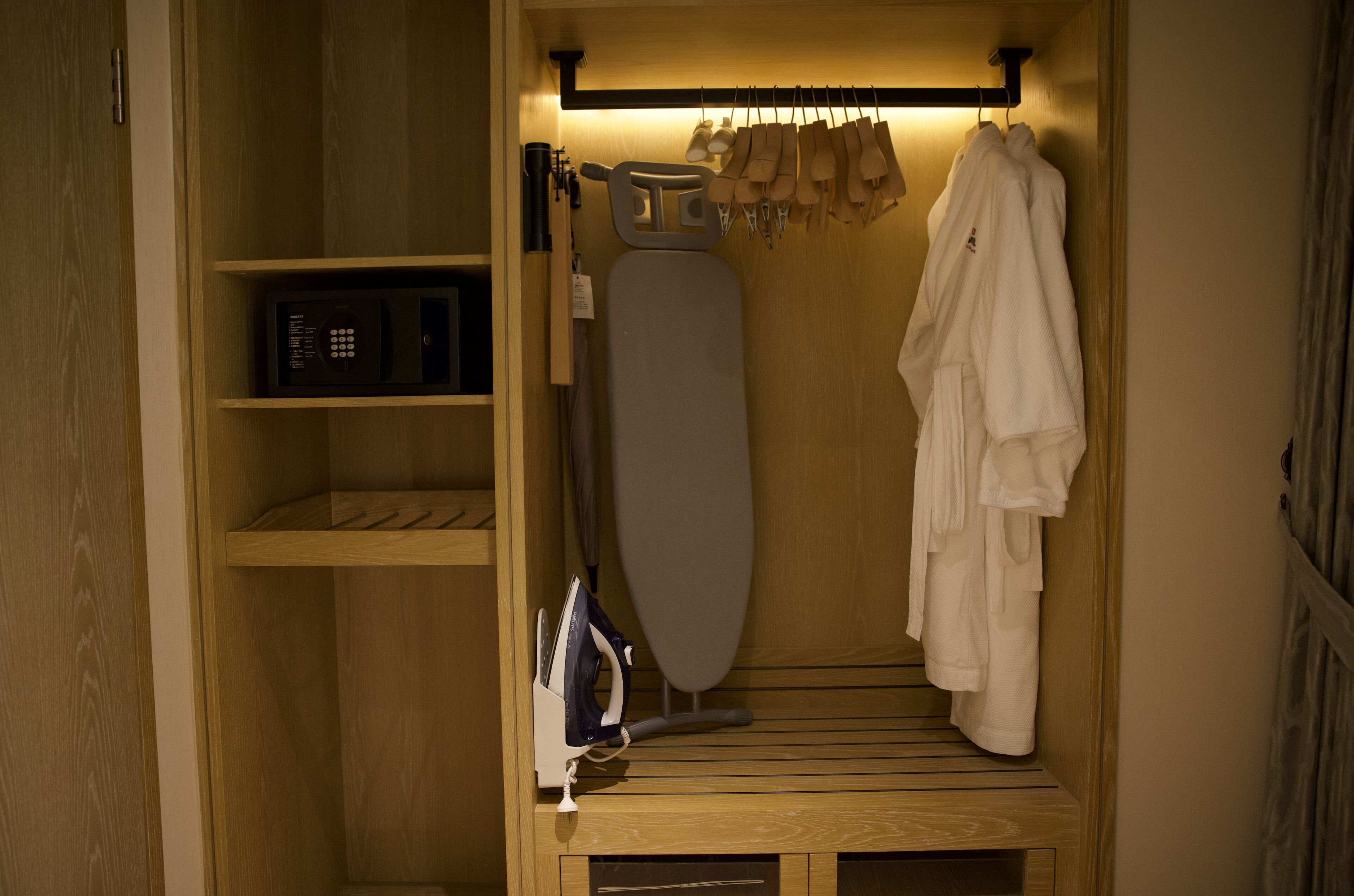 A compact storage unit with a microwave, ironing board, and hanging clothes rack.