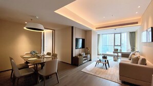 Quarto de hotel moderno com área de refeições, sala de estar e uma grande janela com vista para a cidade.