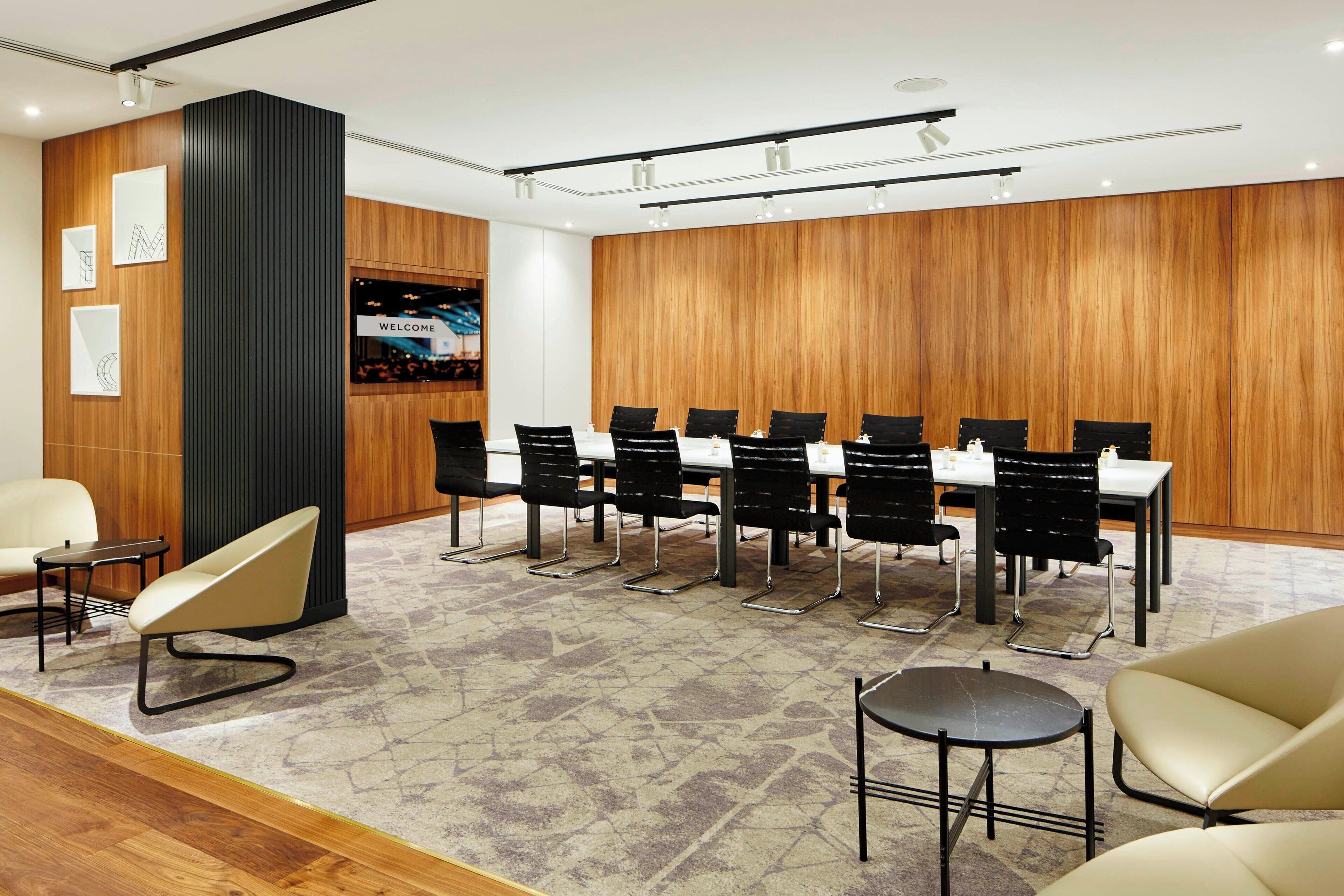 A conference room with a long table, black chairs, and a large screen displaying "WELCOME".
