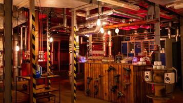 Zona de bar con tuberías expuestas, barra de madera e iluminación de estilo industrial.