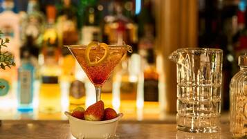 Ein Martini-Glas mit Zitronenscheibe und Erdbeeren auf einer Bar, im Hintergrund ein Krug und Flaschen.