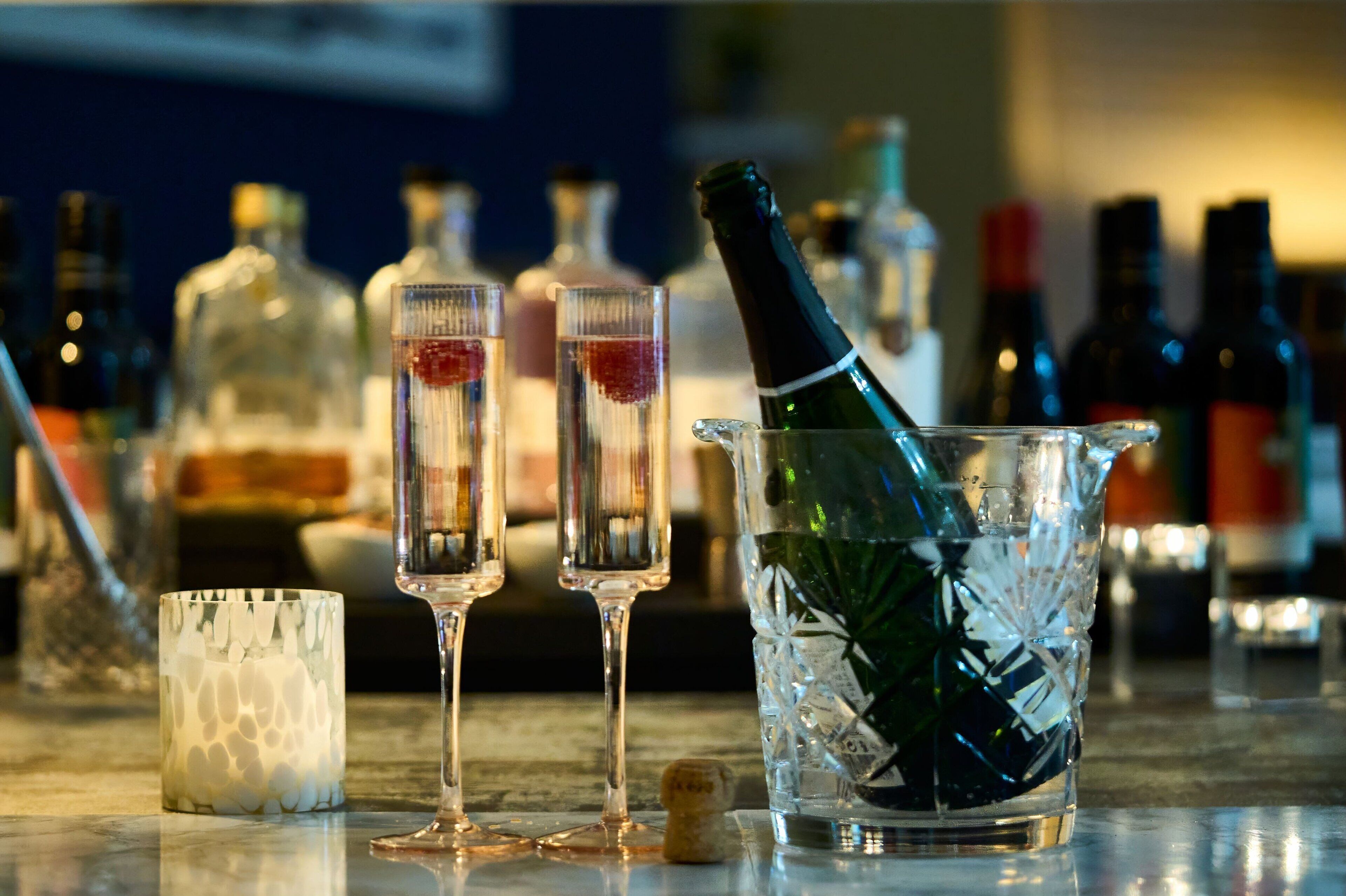 Un'atmosfera da bar con due calici di champagne, una bottiglia in un secchiello e diverse bottiglie sullo sfondo.