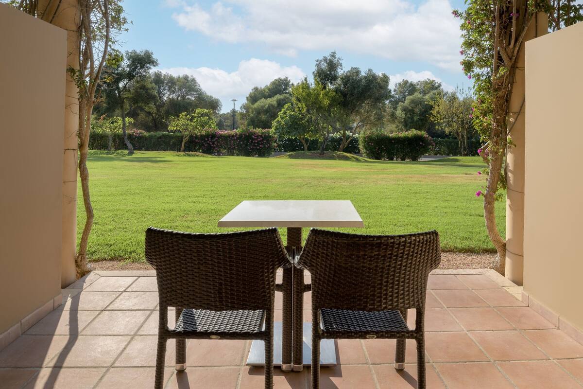 A patio with two wicker chairs and a table, overlooking a well-maintained lawn and trees.