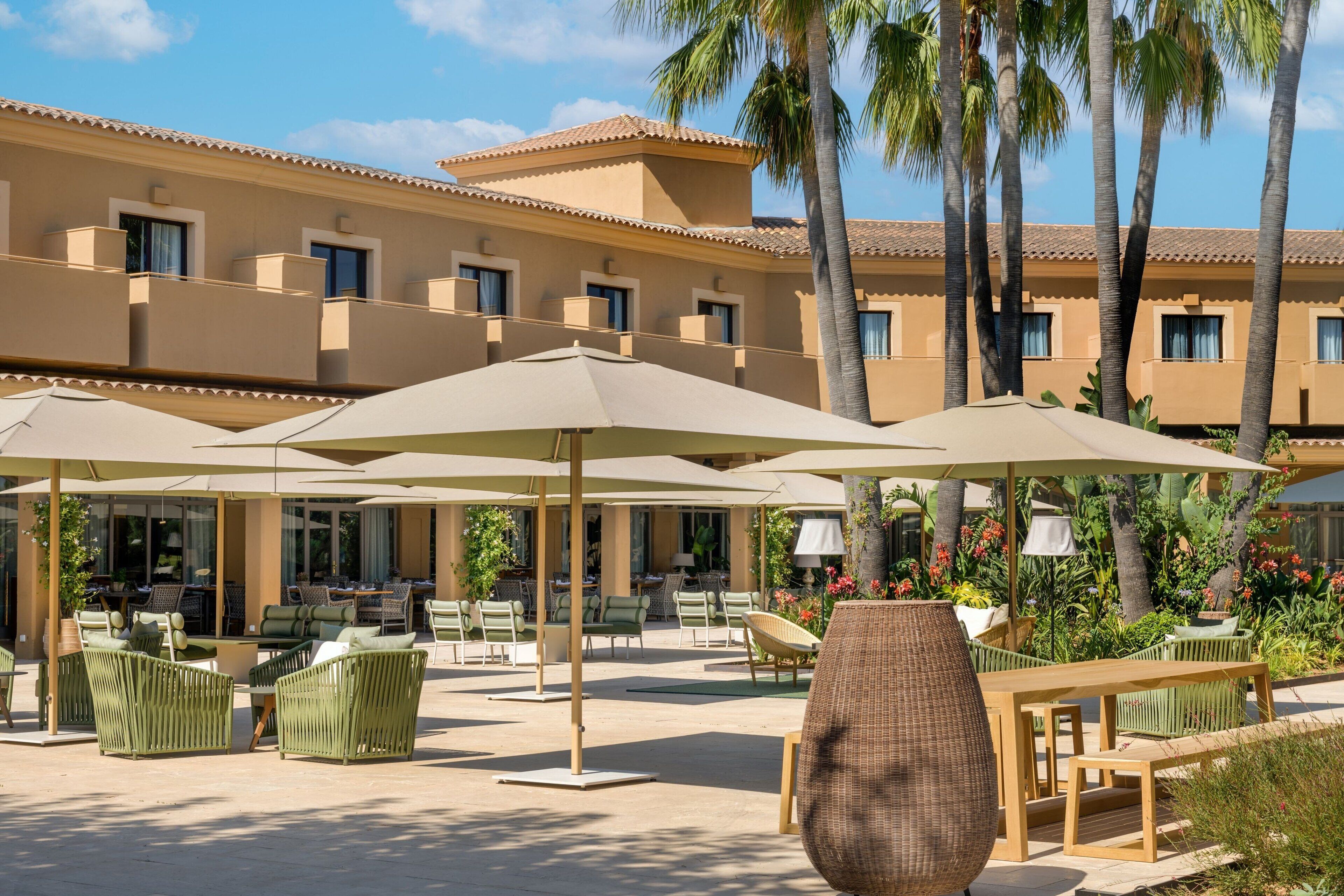 A hotel courtyard with outdoor seating, palm trees, and a building with balconies.