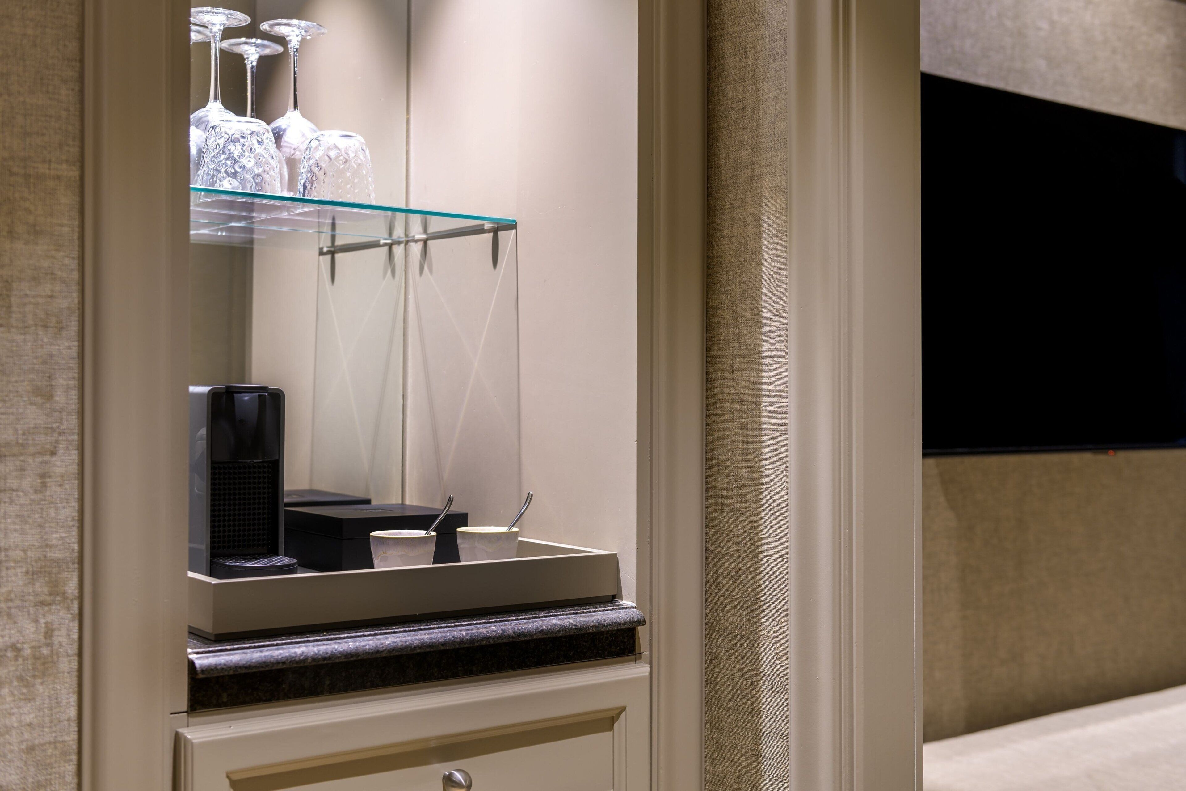 A bathroom vanity with a glass shelf holding decorative items, a coffee maker, and a mirror.