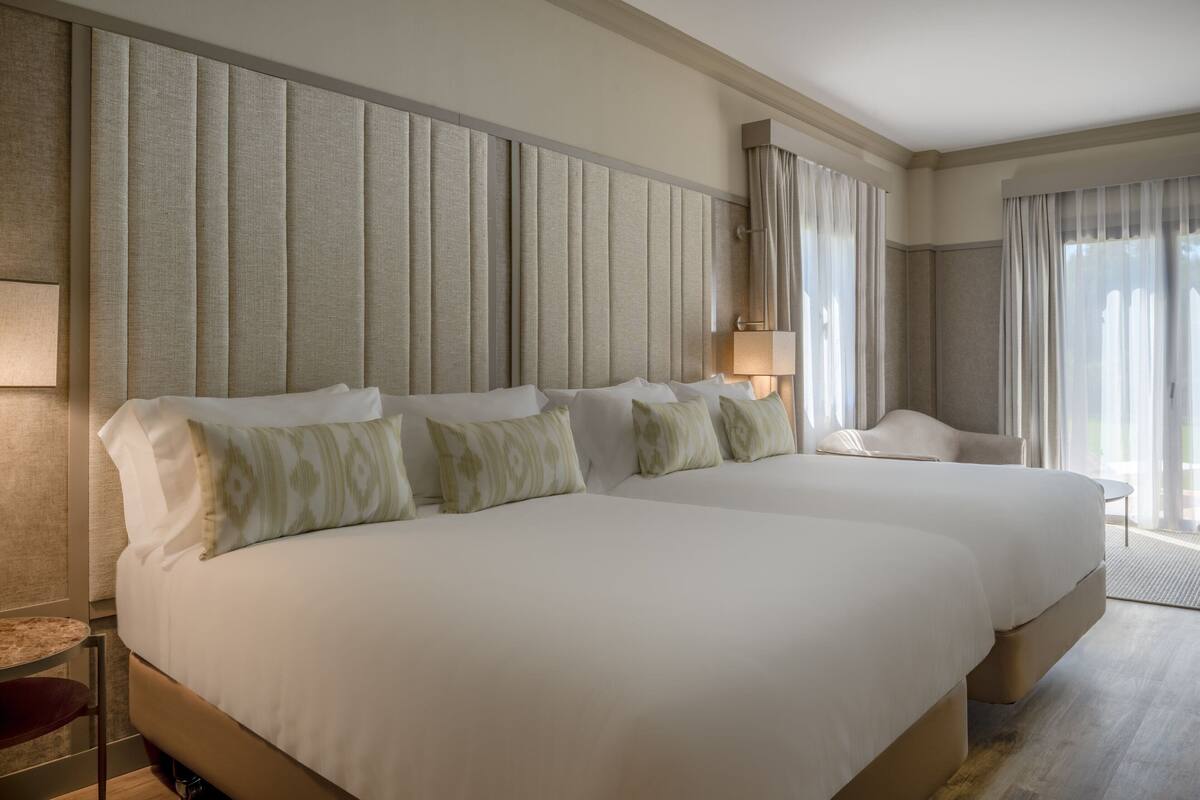 A hotel room with two large beds, a bedside table, a chair, and a lamp.