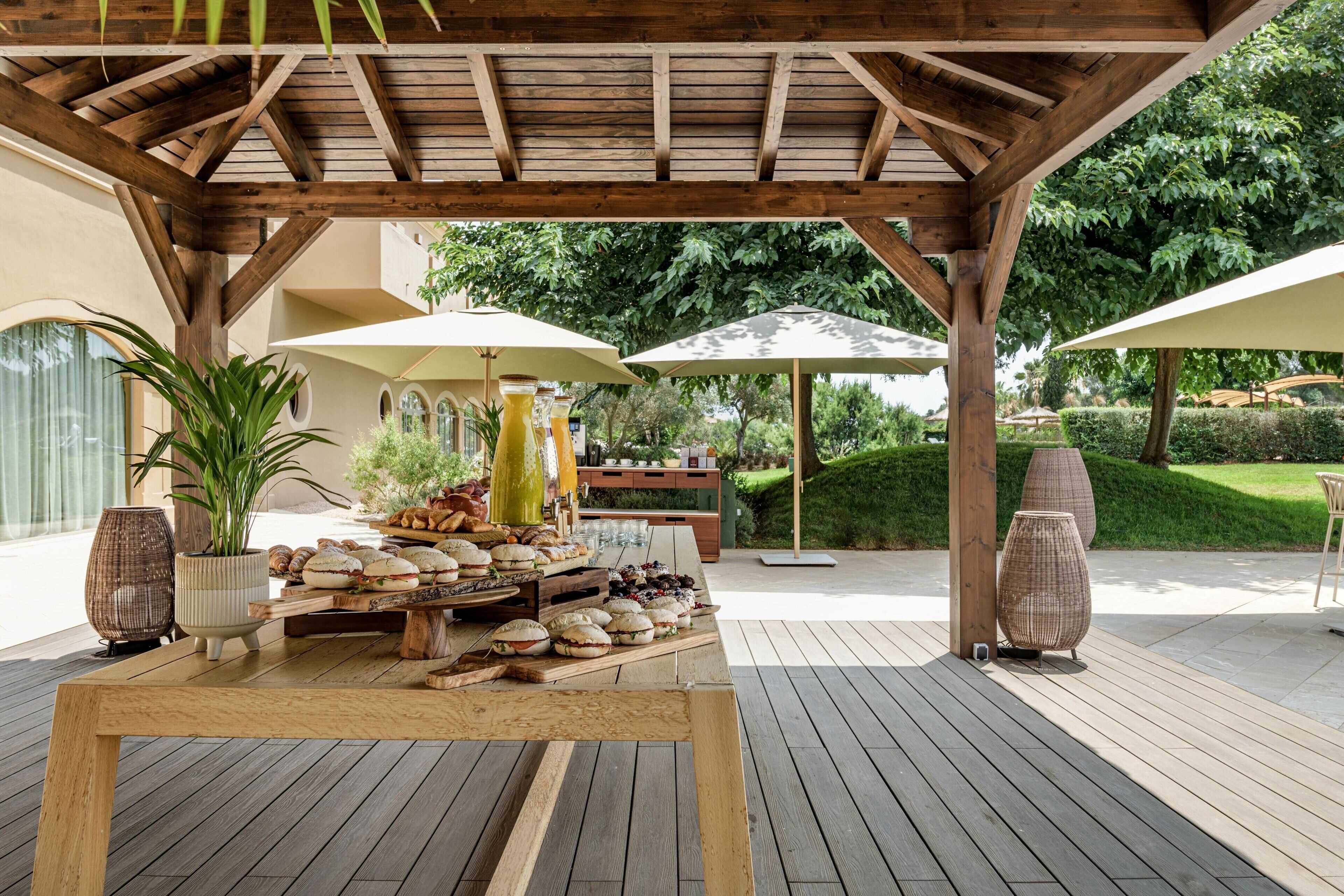 Eine Terrasse im Freien mit Holztischen, Sonnenschirmen und verschiedenen Speisen.