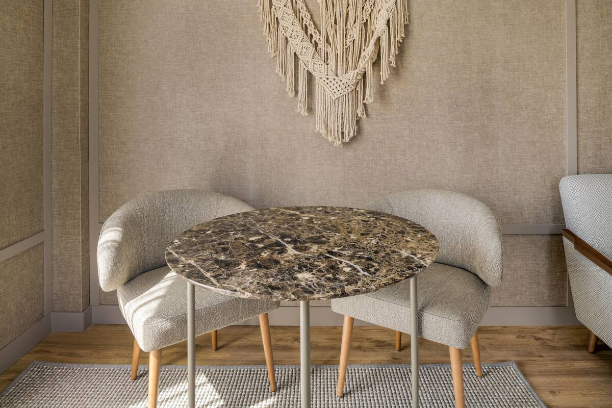 A round table with a marble top, two upholstered chairs, a woven rug, and a macramé wall hanging.