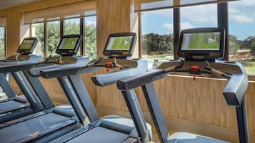 Un gimnasio con cintas de correr, cada una con pantalla digital, en una sala con ventanas amplias y paredes de madera.