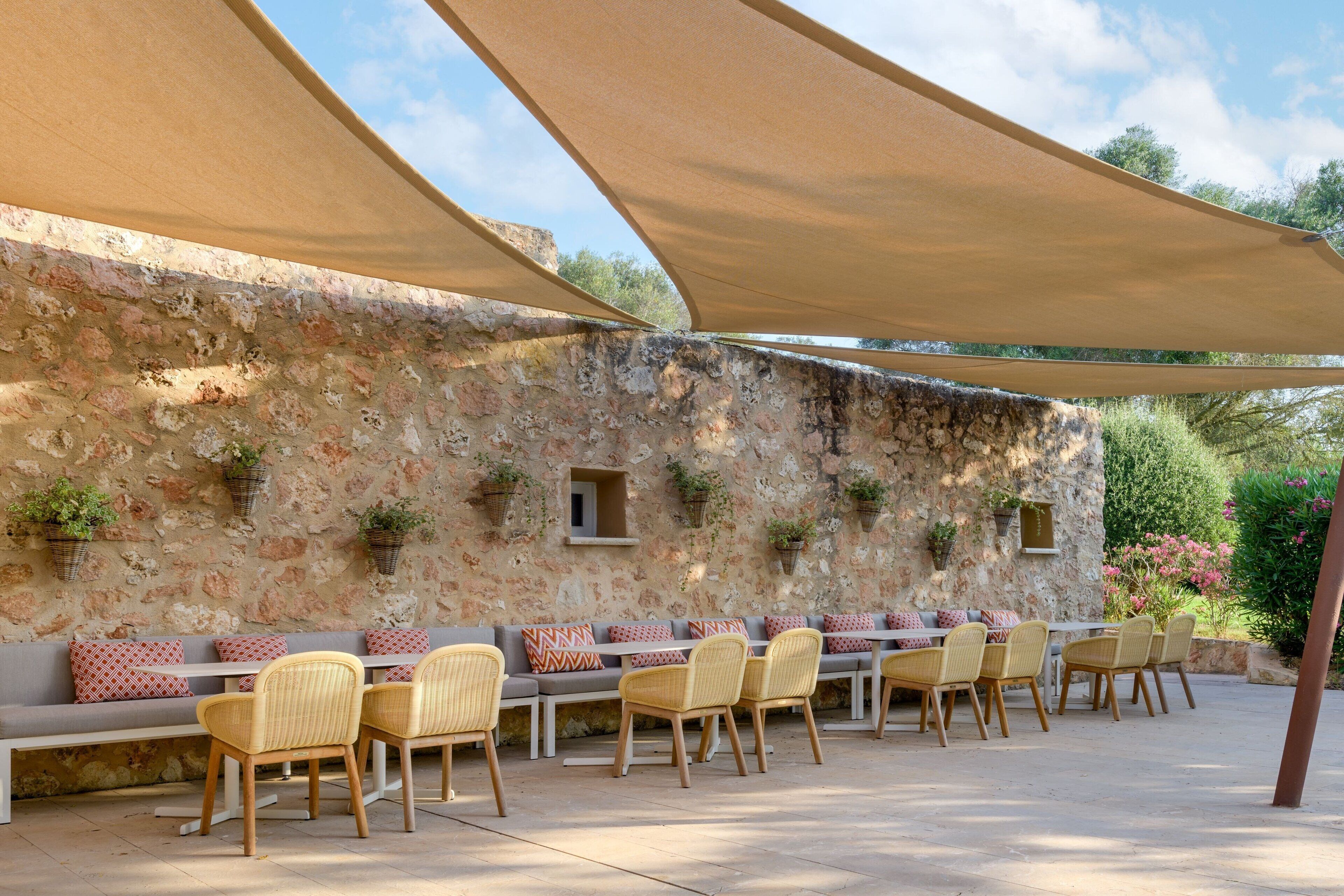 An outdoor seating area with a stone wall backdrop, wicker chairs, and a long bench.