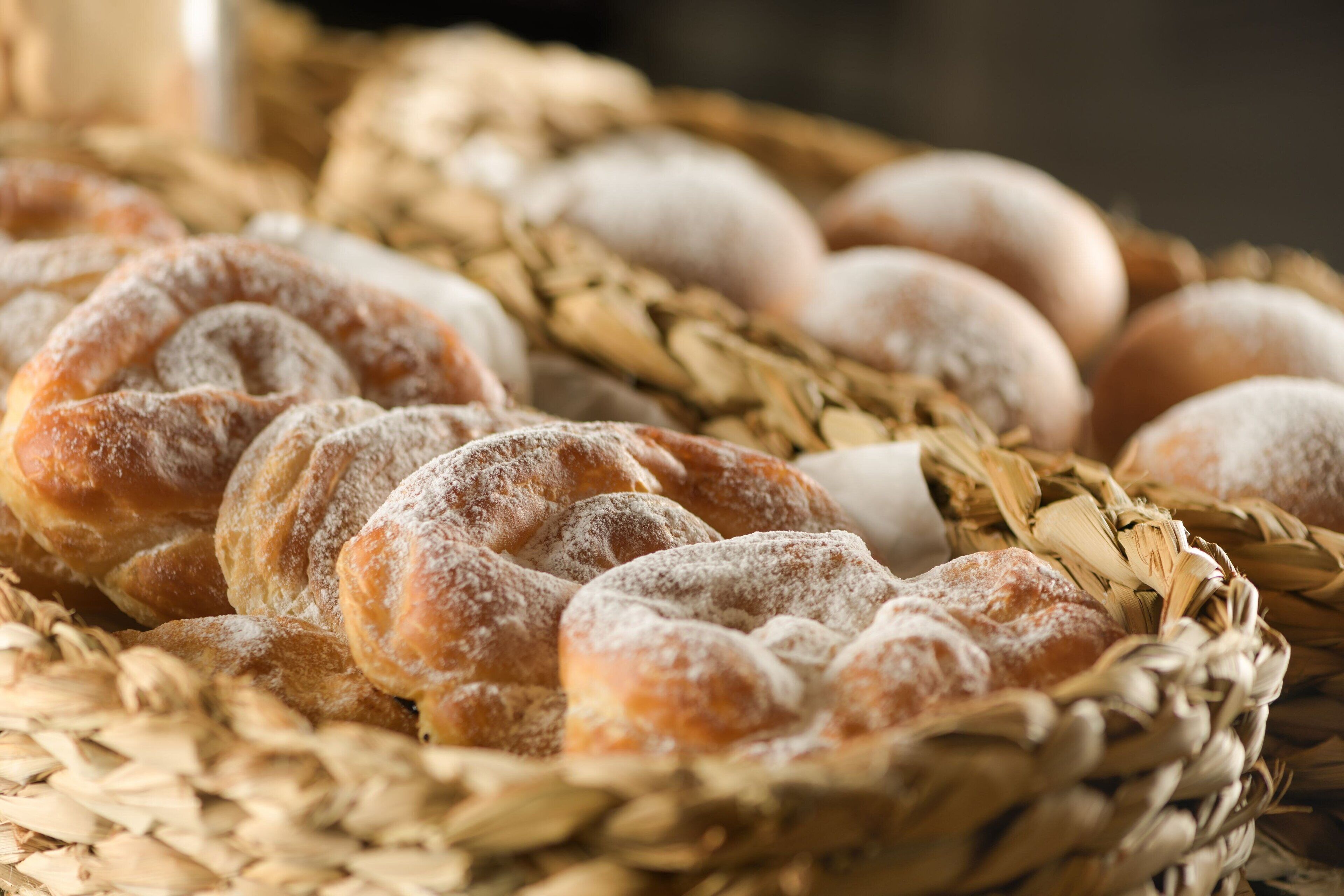 A basket of various breads and pastries, including a braided loaf and round loaves dusted with flour.