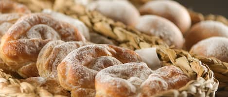 A basket of various breads and pastries, including a braided loaf and round loaves dusted with flour.