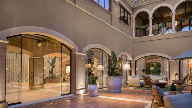 A spacious outdoor area with a seating area, large potted plants, and a glass entrance leading to a lobby. - Hacienda Son Antem Golf Resort, Autograph Collection (Llucmajor)