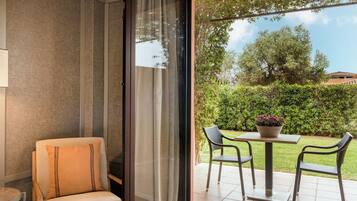 Una habitación con una puerta de vidrio corredera que da a un patio exterior con una mesa y dos sillas, una silla acolchada y una lámpara.