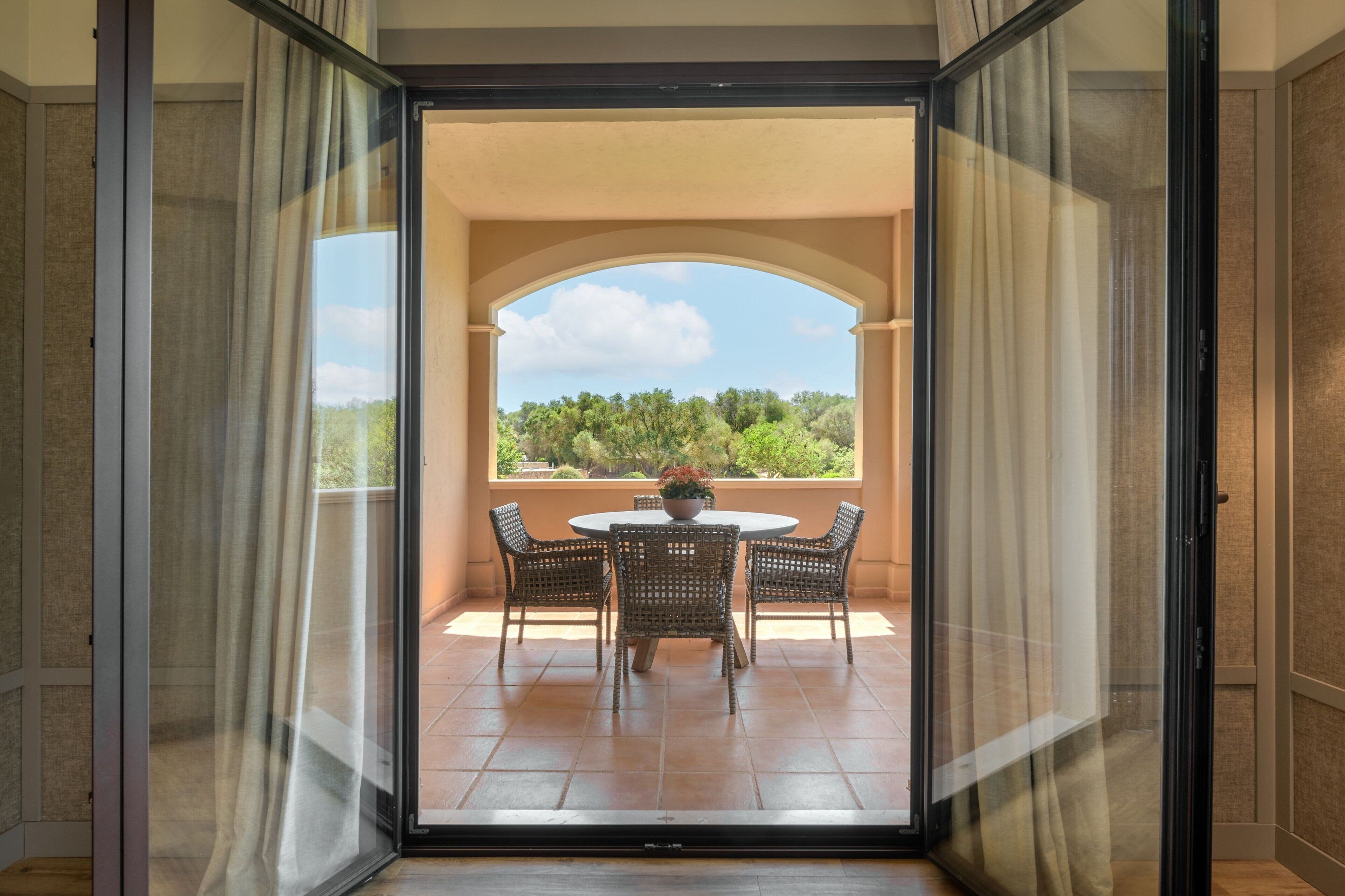 Een balkon met een tafel en stoelen, uitzicht op groen en een heldere lucht.