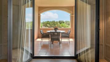 Een balkon met een tafel en stoelen, uitzicht op groen en een heldere lucht.
