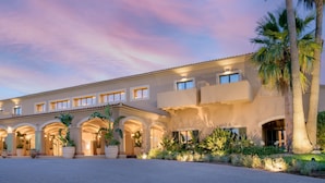 A multi-story hotel with a courtyard, palm trees, and arched walkways. - Hacienda Son Antem Golf Resort, Autograph Collection (Llucmajor)