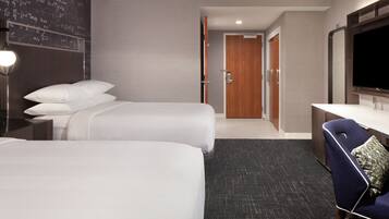 A hotel room with two beds, a desk, a chair, a TV, and a door leading to a bathroom.