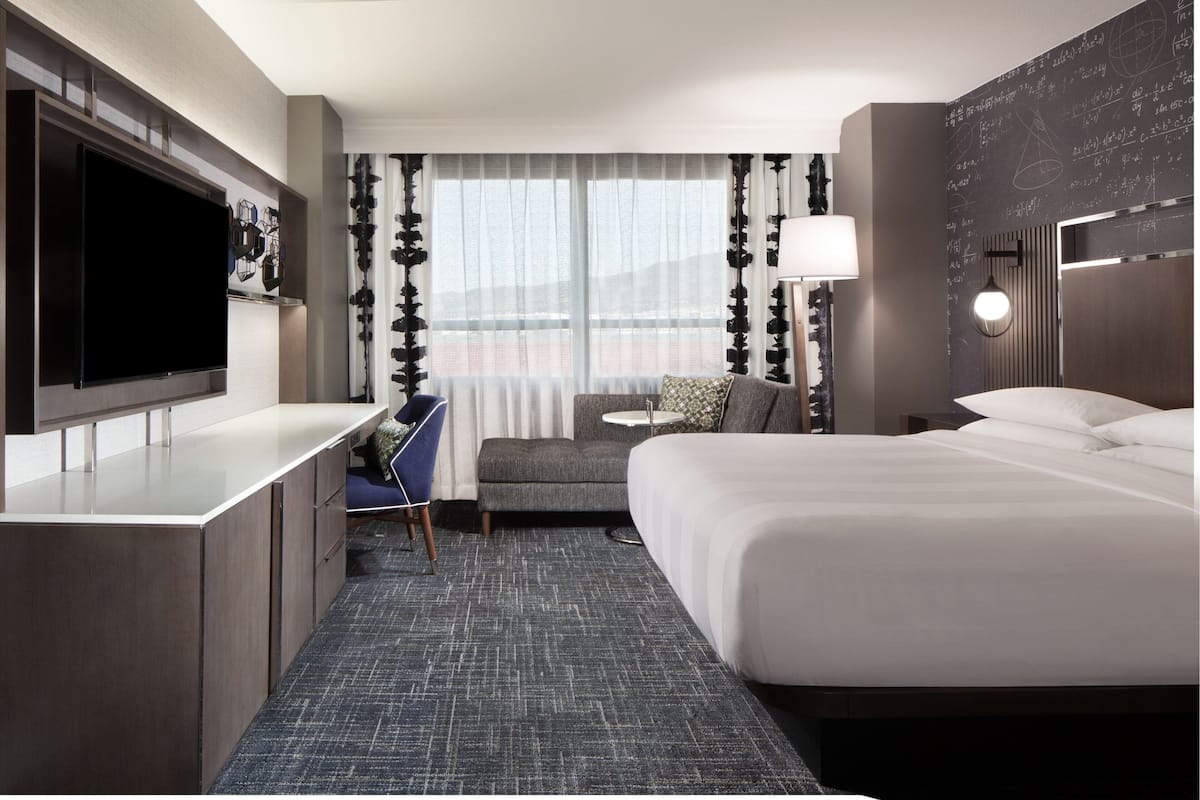 Habitación de hotel con una cama grande, un escritorio con televisión de pantalla plana, un sofá y una mesita de noche con lámpara.