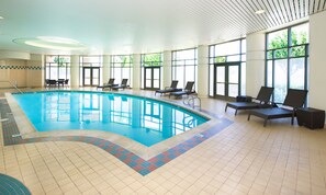 A large indoor swimming pool with clear blue water, surrounded by lounge chairs and large windows allowing natural light. - Fremont Marriott Silicon Valley (Fremont)