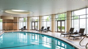 Une piscine dotée de chaises longues et de grandes fenêtres.