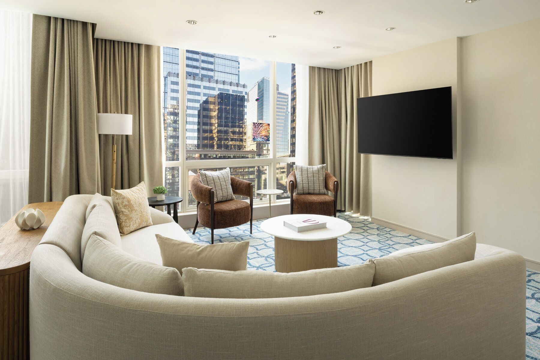 Habitación de hotel con un sofá grande, dos sillones, una mesa de centro y un televisor montado en la pared.