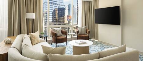 Habitación de hotel con un sofá grande, dos sillones, una mesa de centro y un televisor montado en la pared.