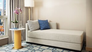 A hotel room with a beige sofa, a small side table with a lamp, a vase with flowers, and a patterned rug. - Millennium Premier Hotel New York Times Square (New York)