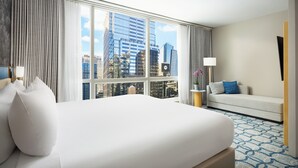 A hotel room with a large bed, a sofa, a TV, and a window with a city view. - Millennium Premier Hotel New York Times Square (New York)