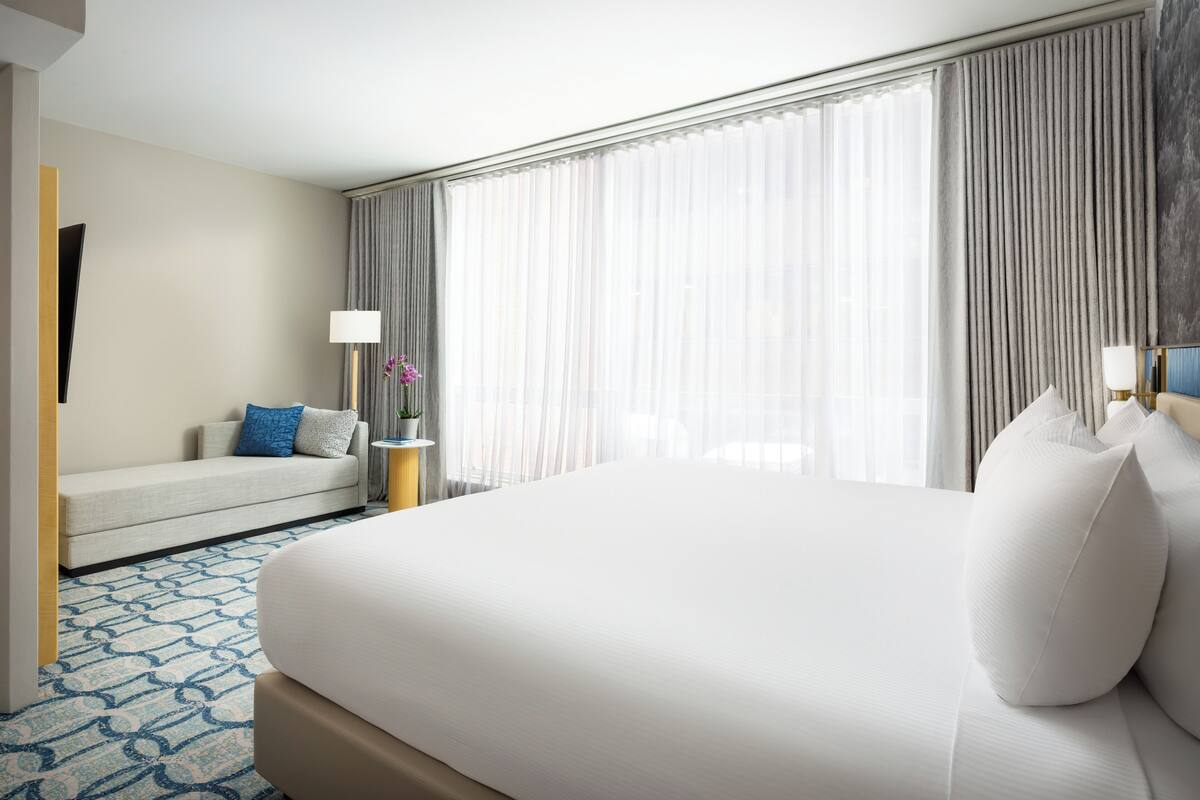 Een hotelkamer met een groot bed, een bank, een lamp en uitzicht op het omliggende landschap.
