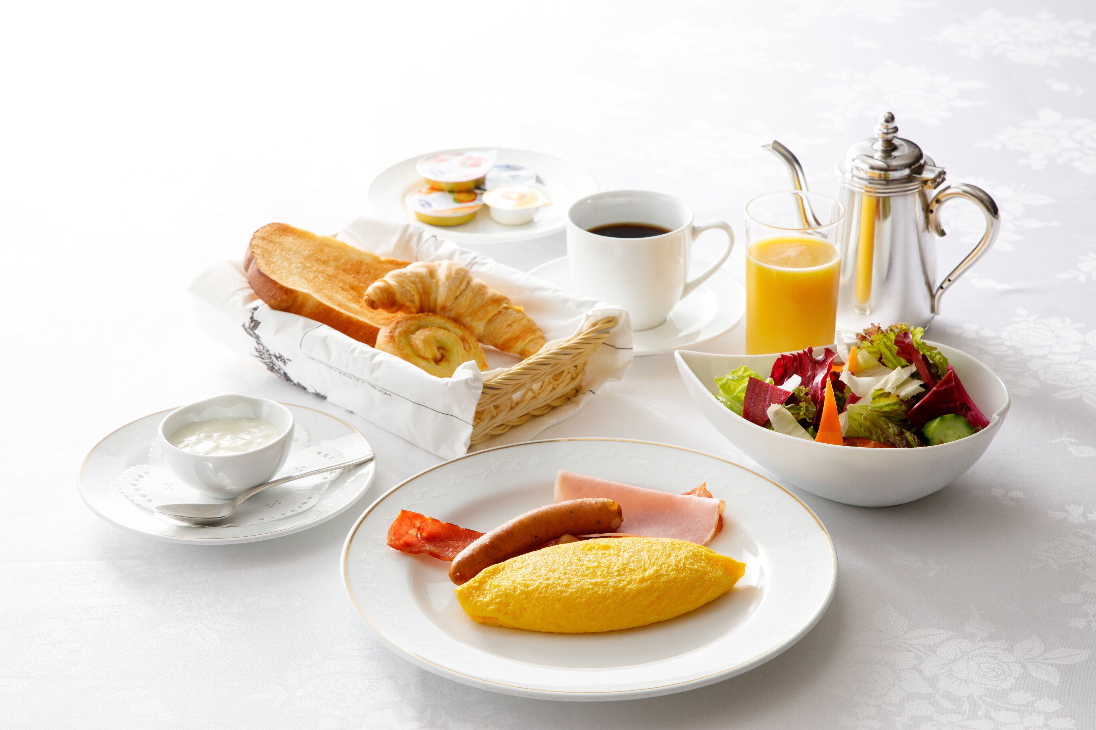 A breakfast setting with croissants, ham, an omelette, a salad, coffee, and orange juice.