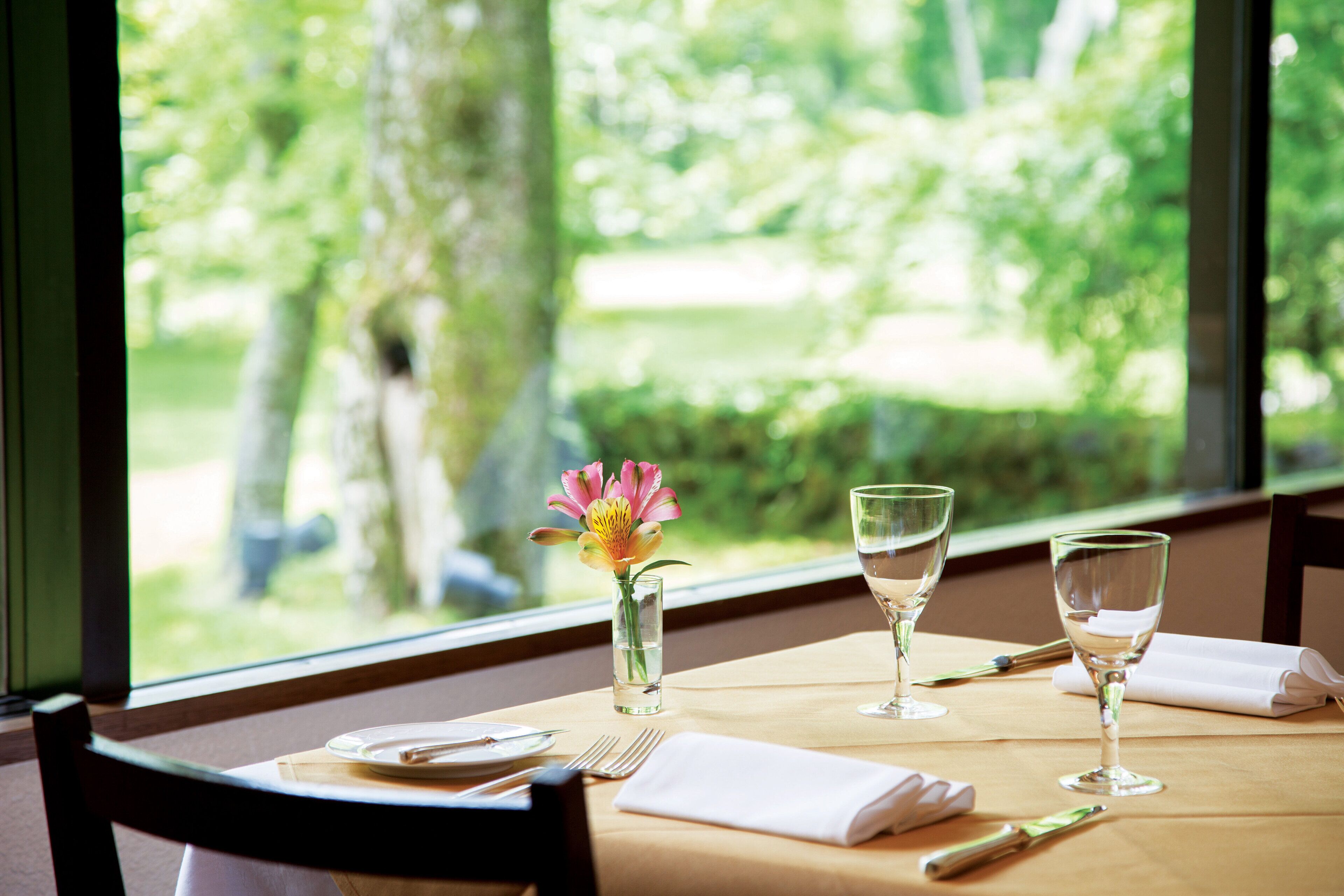 A dining table set with a vase of flowers, two wine glasses, and cutlery.