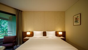 Habitación de hotel con una cama grande, dos mesitas de noche con lámparas, una silla y vistas a zonas verdes.