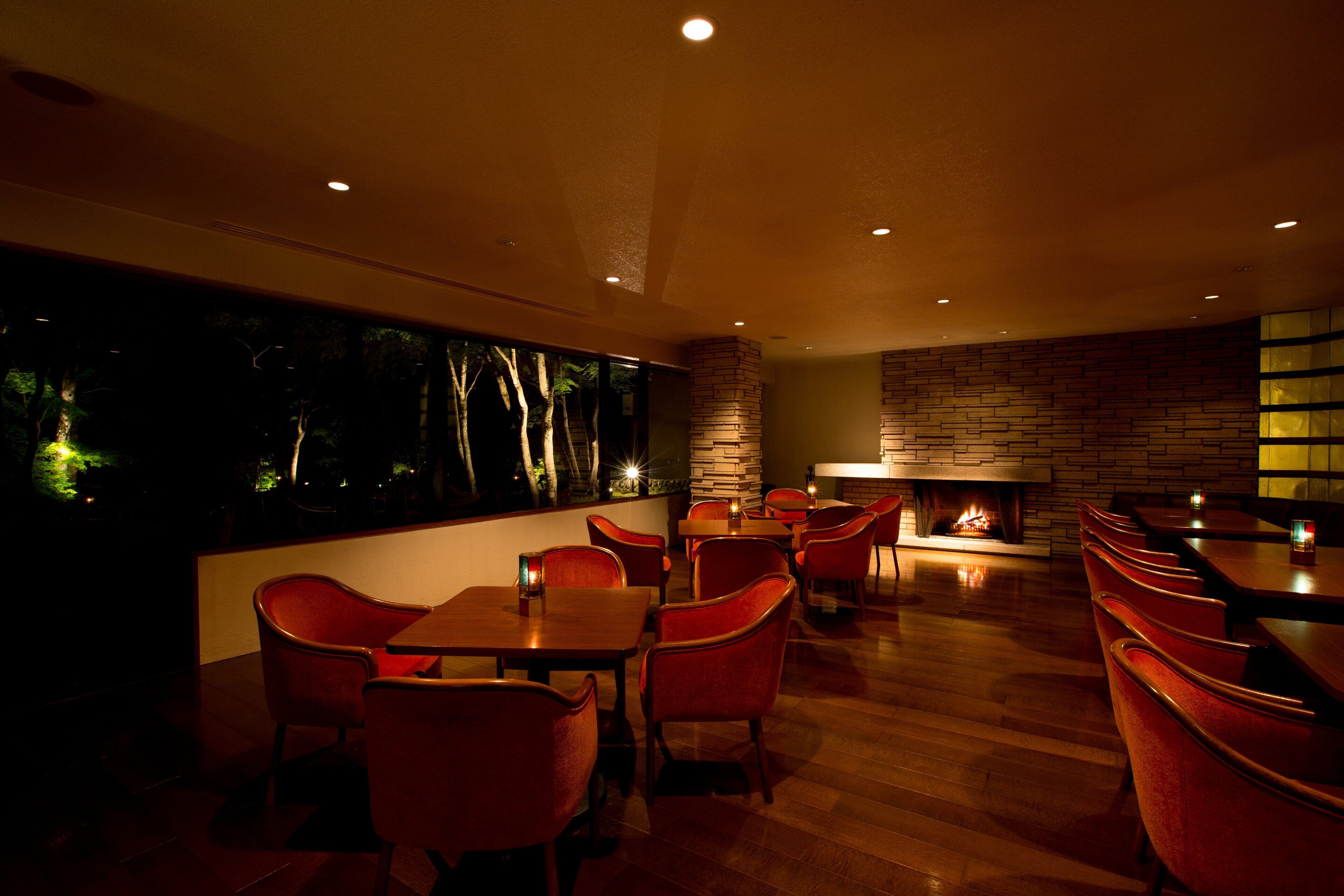 A restaurant with wooden flooring, red chairs, and a fireplace.