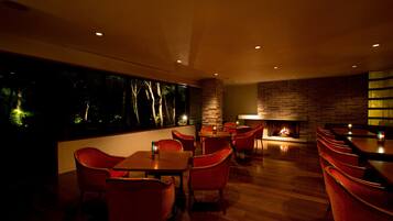 A restaurant with wooden flooring, red chairs, and a fireplace.