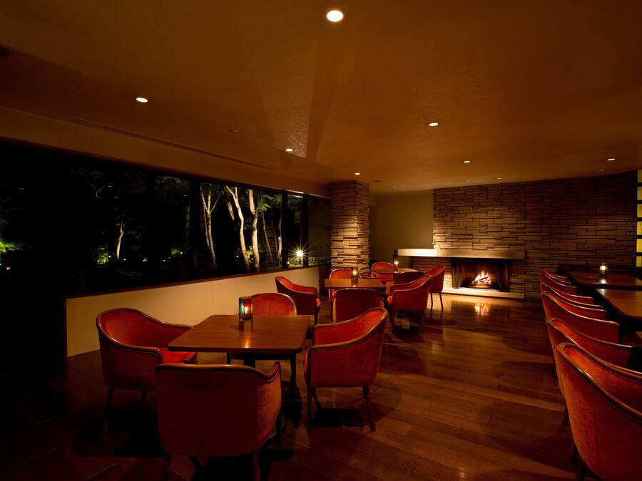 A restaurant with wooden flooring, red chairs, and a fireplace.