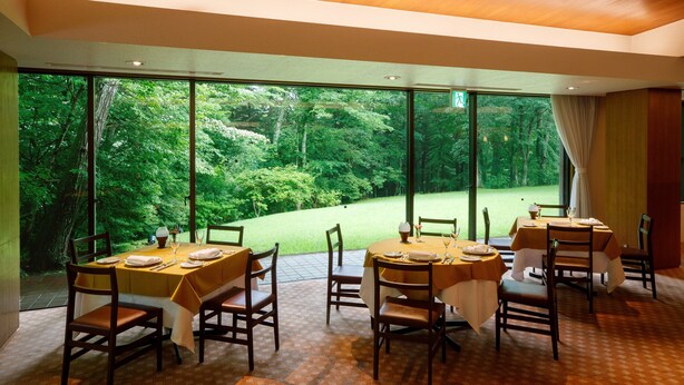 Un comedor con mesas dispuestas para cuatro personas, amplias ventanas que ofrecen vistas a un jardín exuberante.