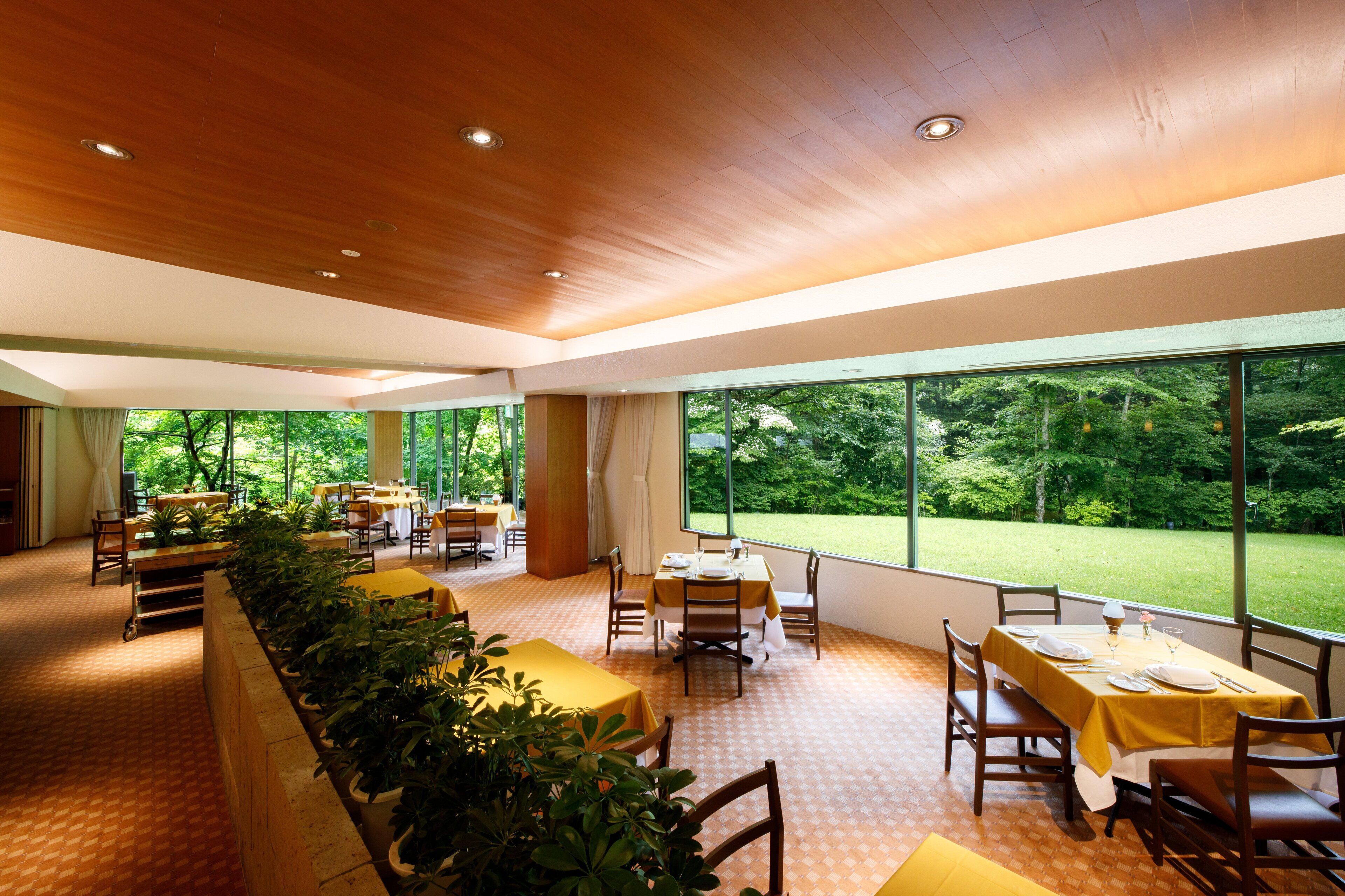 A spacious dining area with multiple tables and chairs, large windows offering a view of a lush garden.