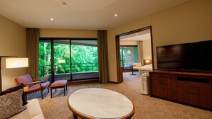 Habitación de hotel moderna con un televisor grande, asientos cómodos, un balcón con vistas y suelo alfombrado.