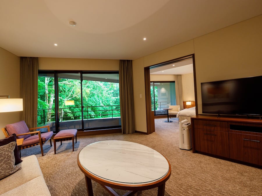 Une chambre d’hôtel moderne dotée d’une grande télévision, de sièges confortables, d’un balcon avec vue et d’un sol recouvert de moquette.