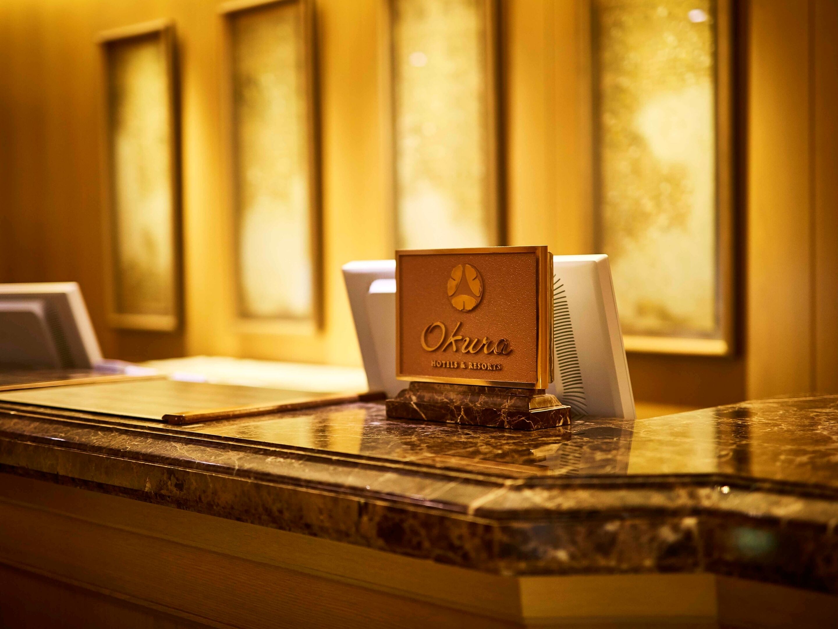 Un mostrador de recepción con un cartel que dice "Okura Hotels & Resorts" y un ordenador portátil sobre la encimera.