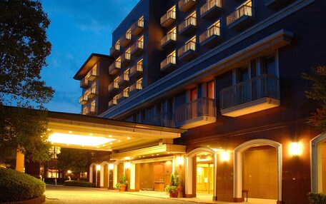A multi-story hotel with a covered entrance, potted plants, and a brick-paved driveway.