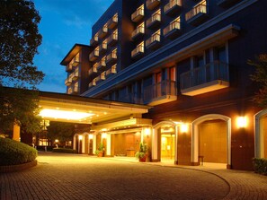 Un hotel de varios pisos con un acceso cubierto, plantas en macetas y un camino de entrada empedrado con ladrillos.